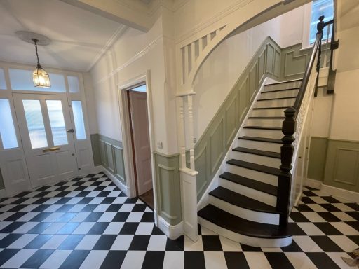 a photo of a ground floor hallway. the flooring is black and white check, the walls are white with green panels